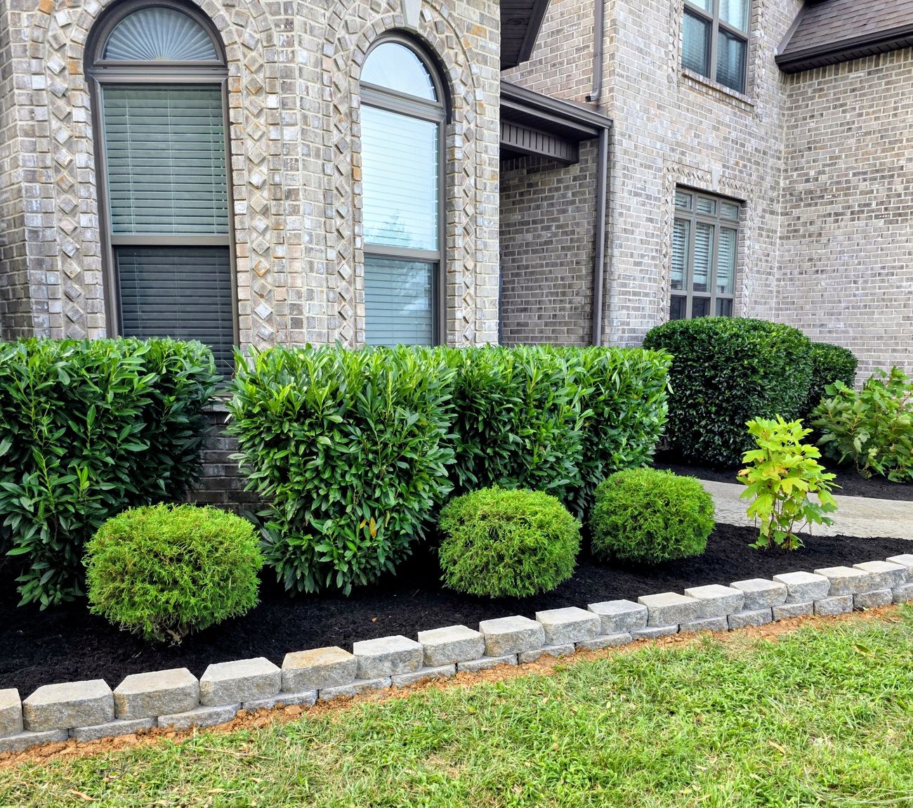 Stone-edged mulch bed with layered shrubs along a brick home
