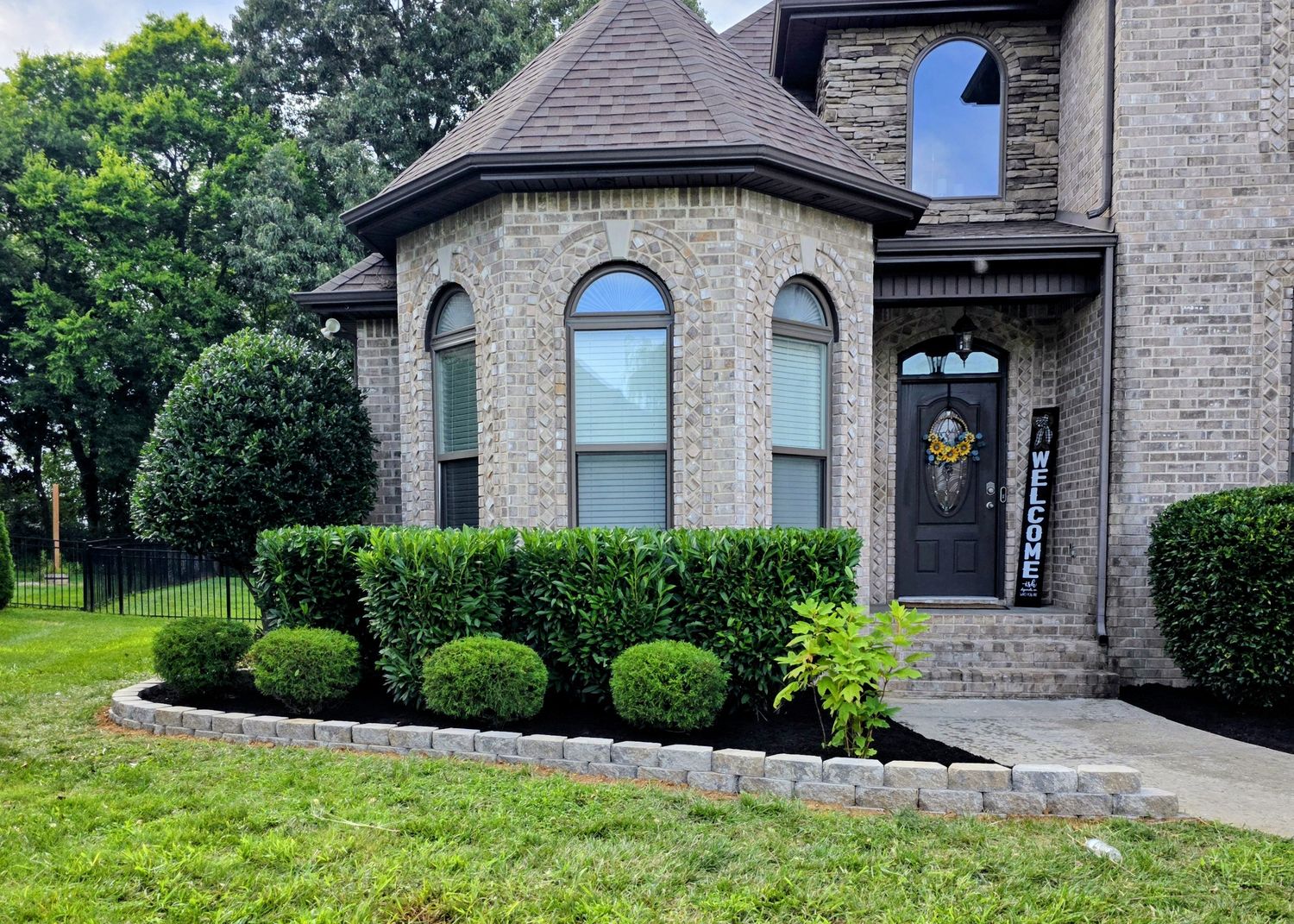 Cobble-edged mulch bed and clipped shrubs across the front of a brick home